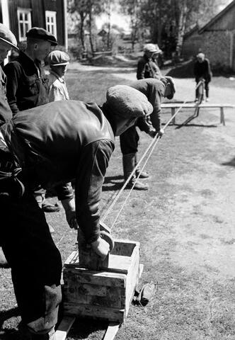 Ryhmä miehiä punoo köyttä maatalon pihalla. 