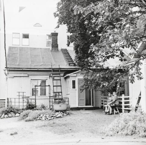 Två gamla kvinnor sitter på en bänk på en innergård. 