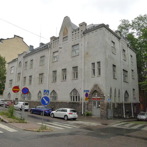 Vanha rakennus, jonka edessä kadun varteen pysäköityjä autoja.