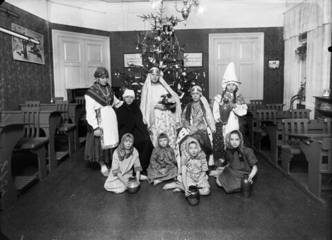 Barn med orientaliska dräkter i en skolklass. Julgran i bakgrunden.