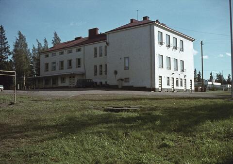 koulurakennus nurmikentän takana, tuuletusikkunat ovat auki.