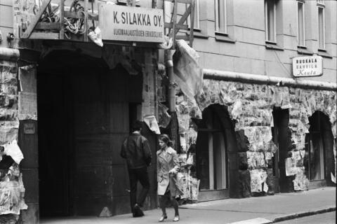 Kruunuvuorenkatu 1:n kerrostalon maalaustöiden ajaksi sanomalehdillä suojattu kivijalka. Porttikäytävän yläpuolella Ulkomaalaustöiden erikoisliike K. Silakka Oy:n maalarinkelkka. Oikealla Ruokala Kahvila Keulan kyltti.