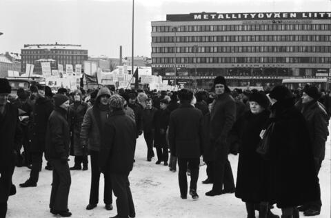 Ihmisjoukko seisoo talvisella Hakaniemen torilla Metalliliiton mielenosoituksessa. Taustalla Metallitalo, jonka katolla lukee suurin kohokirjaimin Metallityöväen Liitto.
