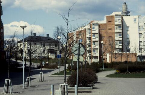 Näkymä Pasilan puistotieltä. Oikealla uusi, punatiilinen asuinkerrostalo, vasemmalla vanha kaksikerroksinen puutalo.