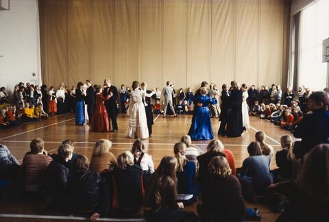 Gammeldans på gång i skolans festsal. Skolans yngre elever sitter i ring runt dansgolvet. 