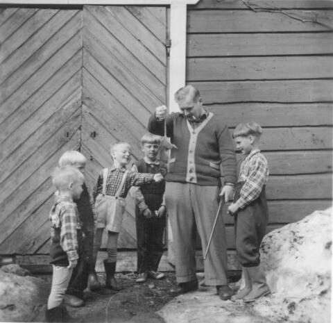Mies piippu suussa roikottaa hännästä kuollutta rottaa. Pikkupoikien lauma osoittelee eläintä.