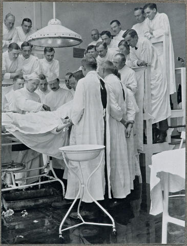 Parikymmentä henkilöä, ilmeisesti lääketieteen opiskelijaa, seuraa leikkausta leikkauspöydän ympärillä. Valtaosa heistä seisoo porrastettujen penkkirivien päällä.