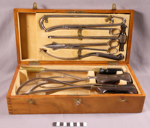 Olika metallinstrument som behövdes i förlossningar i en trälåda fodrad med gulaktig sammet. Lådan är försedd med lås och nyckel.