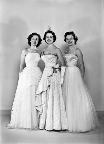 Kolme valkoisiin mekkoihin pukeutunutta missiä hymyilee ryhmäkuvassa.