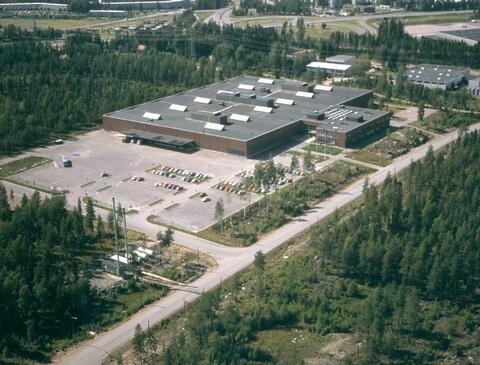 Ilmakuvan keskellä on iso, matala painatuskeskus. Ympärillä on metsikköä ja teitä.