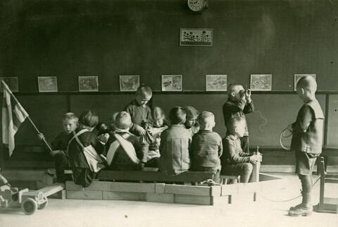 Ryhmä lapsia on rakentanut isoista palikoista "laivan" huoneen lattialle. Kymmenkunta lasta istuu "laivan" kyydissä. 