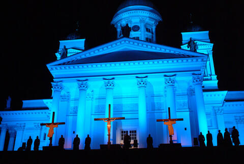 Belyst domkyrka med tre stora kors och åskådare framför