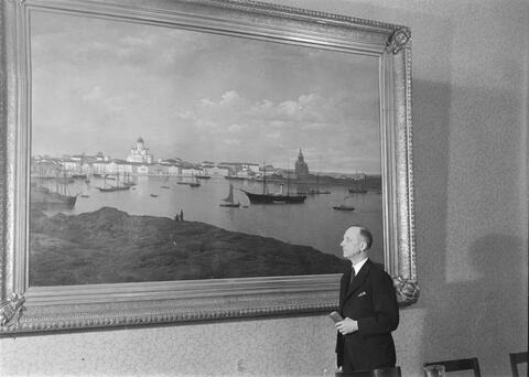 Kaupunginjohtaja Eero Rydman kuvattuna suuren, Helsingin keskustan merimaisemaa esittävän maalauksen edessä.