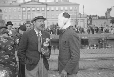 Toimittaja haastattelee miestä, jonka pää on kääritty siteisiin.