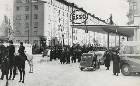 Ratsupoliiseja, autoja ja suuri väkijoukko huoltoasemalla.