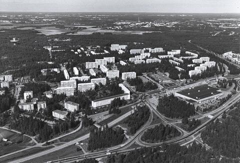 Lähiön kerrostaloja, maanteitä ja metsikköä.