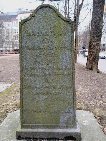 En grå gravvård omgiven av gräs. Det växer alg på vården.