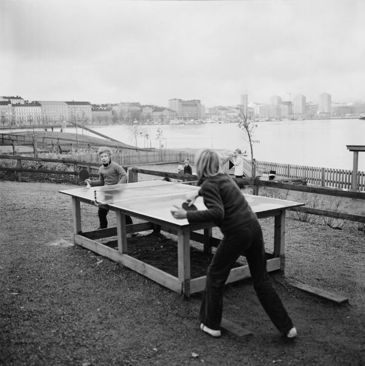Pojat pelaavat pöytätennistä Laivastopuiston leikkipaikalla Katajanokalla. Taustalla rakenteilla oleva Merihaka.