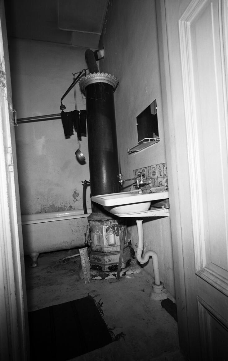 Ränsistynyt pitkänomainen kylpyhuone, jossa takaseinällä on amme. Sen edessä seisoo pylväsmäinen kuumavesivaraaja, ja etualalla on pesuallas.