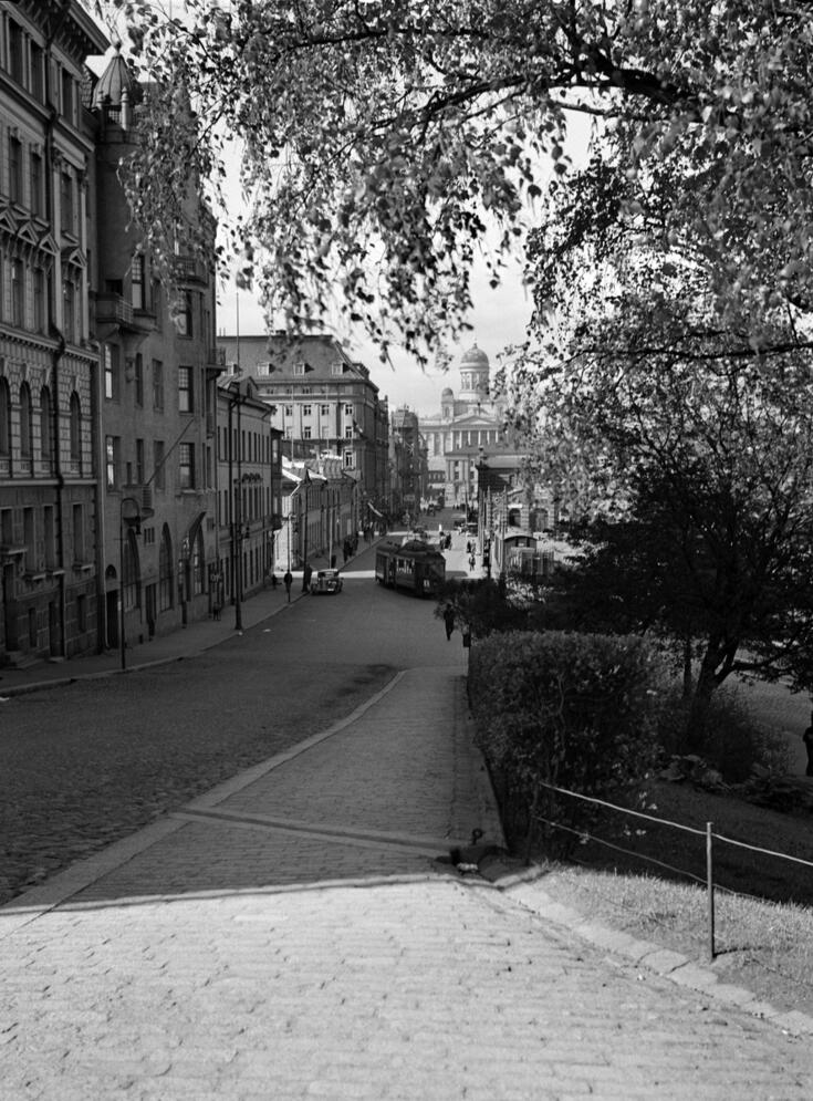 Vasemmalla on Etelärannan rakennukset 6–12, etualalla on mukulakivettyä jalkakäytävää, oikealla puistoa. Taustalla on Vanha kauppahalli ja Tuomiokirkko. Kuvassa on myös raitiovaunu ja tavarajuna. 