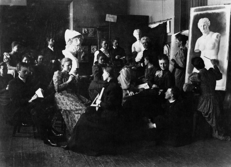 En grupp studerande har samlats i ett klassrum med målningar och skulpturer