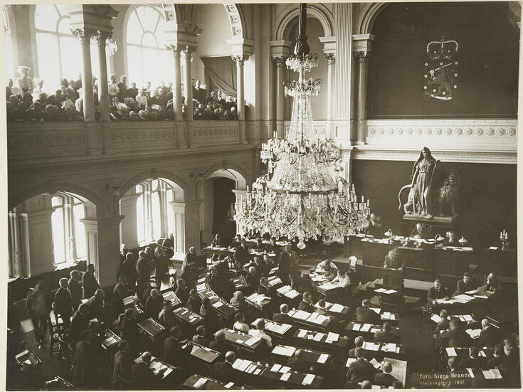 Parvelta otetussa valokuvassa näkyy ihmisiä istumassa pöytien ääressä selin kuvaajaan. Katosta roikkuu suuri kristallikruunu. Tilan edessä seinällä on  Suomen vaakuna ja sen alapuolella veistos, joka esittää naista ja leijonaa.