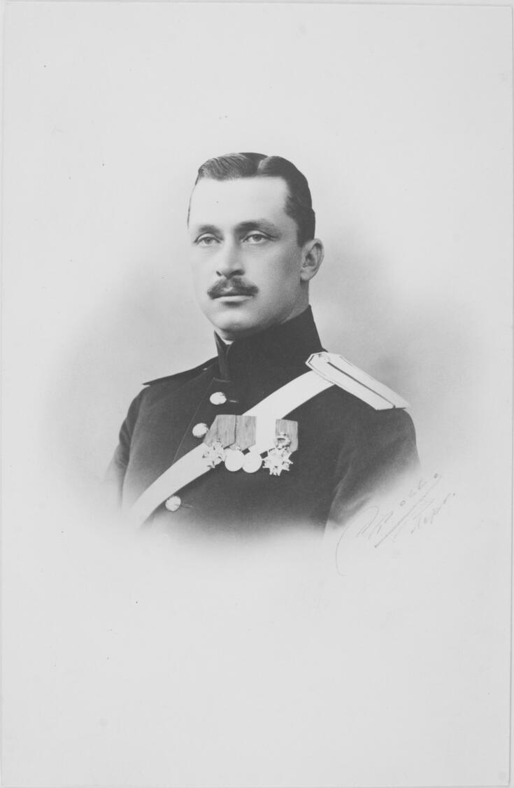 Ratsumestari Gustaf Mannerheimin muotokuva. Kuva on lähikuva ja leikkautuu rinnan kohdalta. Mannerheim on pukeutunut tummaan univormuun. Rinnassa on rivissä neljä kunniamerkkiä ja muistomitalia. Tummat hiukset on kammattu sivujakauksella taakse. Katse on suuntautunut vinosti vasemmalle.