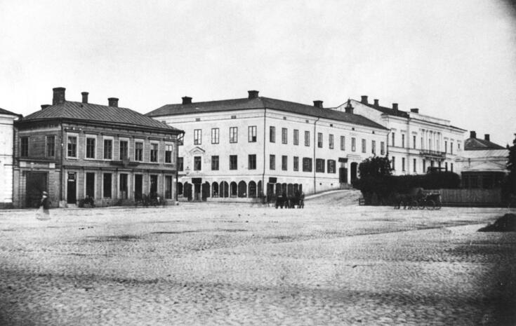 Etualalla on tyhjää mukulakivitoria, taustalla on Eteläesplanadin alkupään 2- tai 3-kerroksiset rakennukset. Ihmisiä ja hevosvaunujakin näkyy.