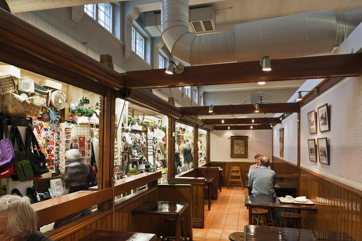 Vasemmalla näkyy myyntikojuja, oikealla kahvilan pöytiä, joissa istuu muutama asiakas.