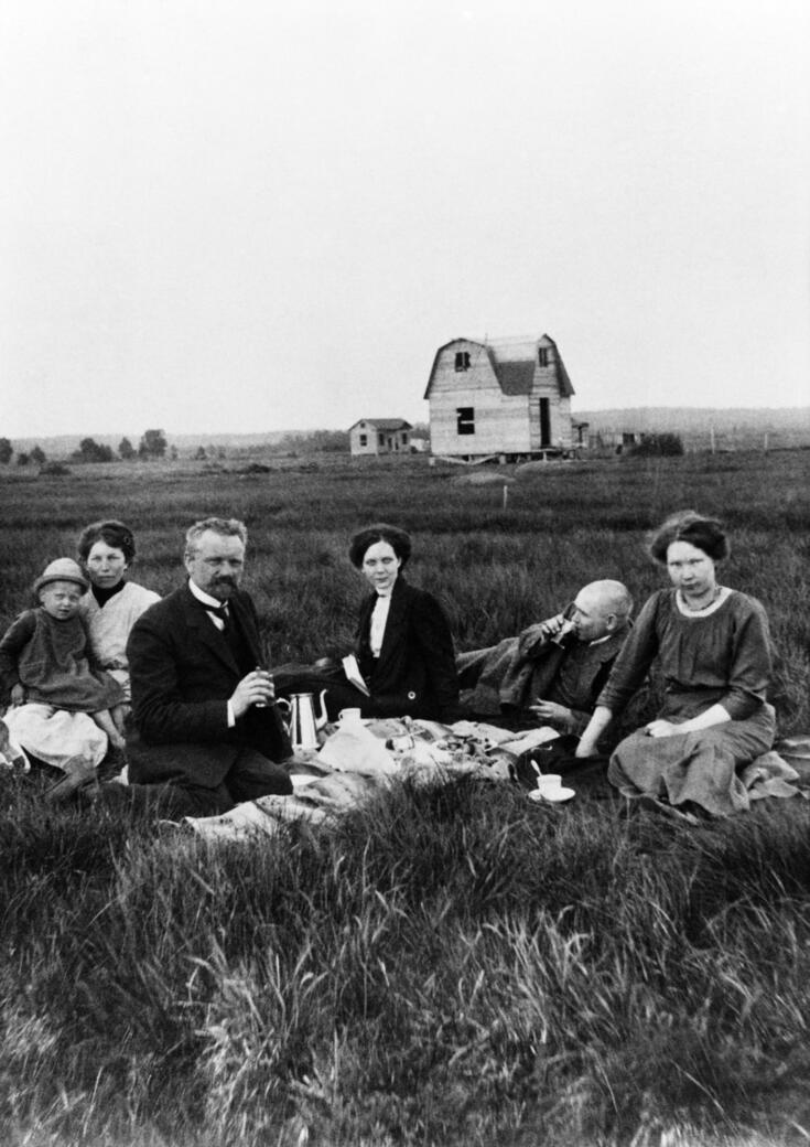 Seurue viettämässä kahvihetkeä pihanurmikolla. Taustalla ilmeisesti Sokoleffin talo rakenteilla