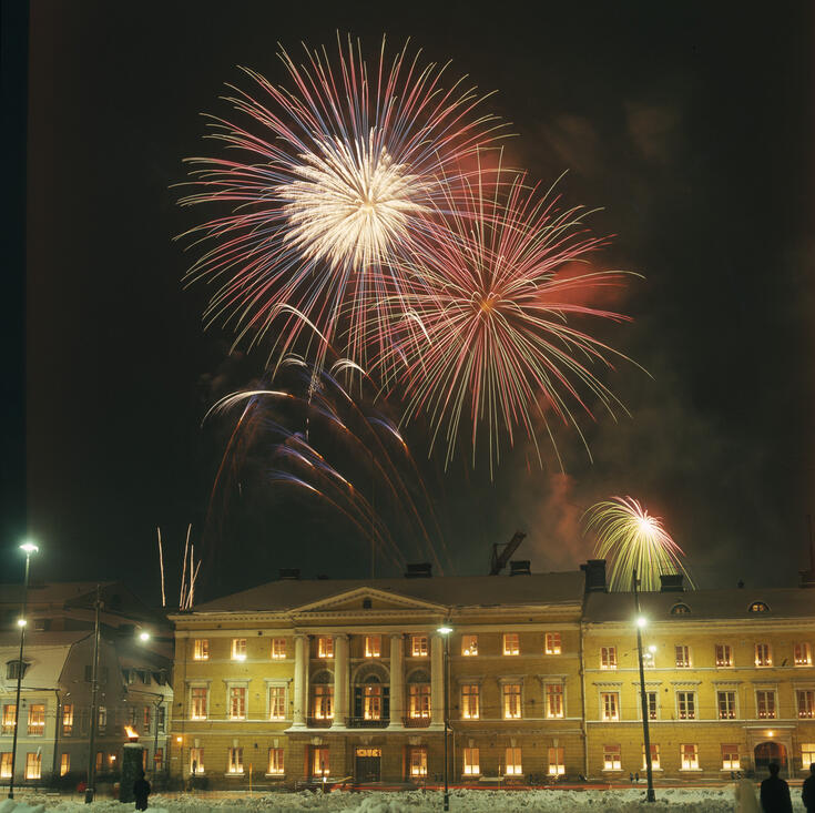 Senaatintorin eteläreunan rakennuksia, joiden ikkunat on valaistu. Taivaalla on ilotulitteita.