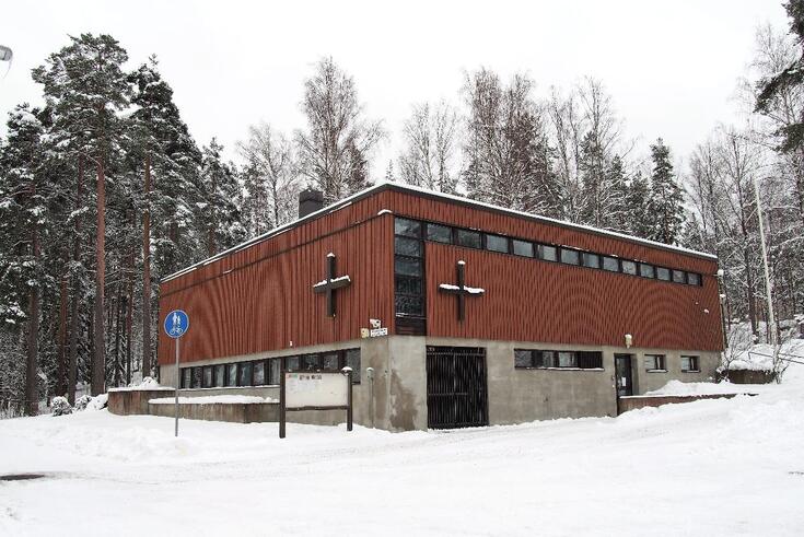 Kulmasta kuvattu laatikon muotoinen rakennus, jonka alaosa on betonia ja yläosa punatiiltä. Yhden seinän vasemmassa reunassa sekä yläosassa on nauhamainen rivi pieniä ikkunoita. Kahdessa ulkoseinässä on plusmerkin näköinen risti.