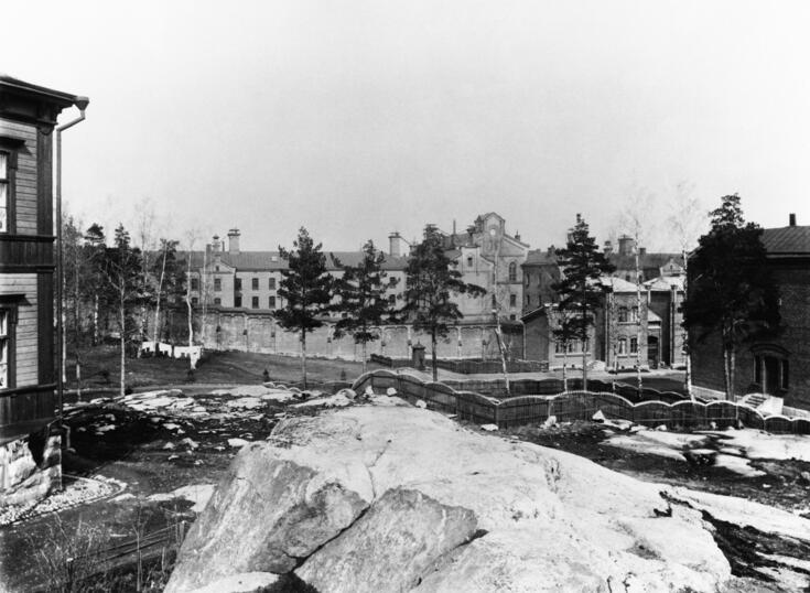 Etualalla on kalliota, taaempana puita, rakennuksia ja vankilan muuria. 