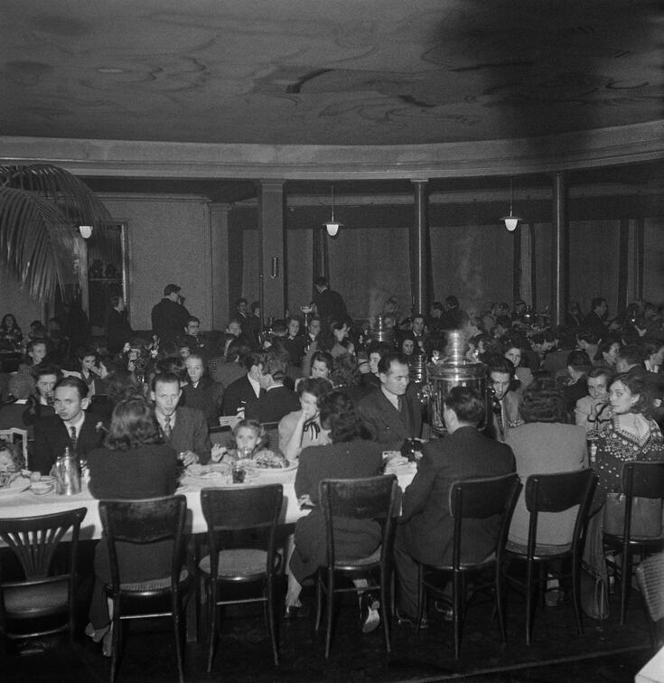 En rund restaurangsal fylld med familjer vid långa bord. 