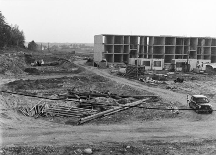 Rakennustyömaa, jolla myös lapset leikkivät rakennusmateriaaleilla. Taustalla on kolmikerroksisen elementtitalon runko.