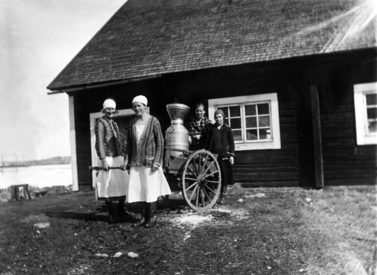 Ladugårdspersonal har samlats framför en låg stockbyggnad med en mjölkkärra.