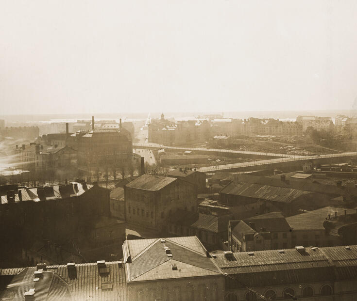 Näkymä Rautatieaseman tornista länteen kohti Arkadiankatua. Vasemmalla Arkadiankadun kulmassa on Hankkijan pääkonttori (ent. Nikolajeffin autoliike, arkkitehti Jarl Eklund 1913) ja sisällissodassa vaurioitunut Turun kasarmin rakennus. Läntinen Viertotie (nyk. Mannerheimintie) kulkee kuvassa poikittain vasemmalta oikealle. Sen takana oikealla näkyy Etu-Töölön Nervanderinkadun asuinkerrostaloja, joiden edessä sijaitsevalle kallioiselle Arkadianmäelle rakennettiin Eduskuntatalo vuosina 1926–1931. 