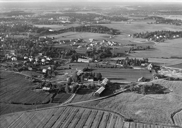 Ilmakuva, jossa etualalla peltoja ja keskellä maatila. 