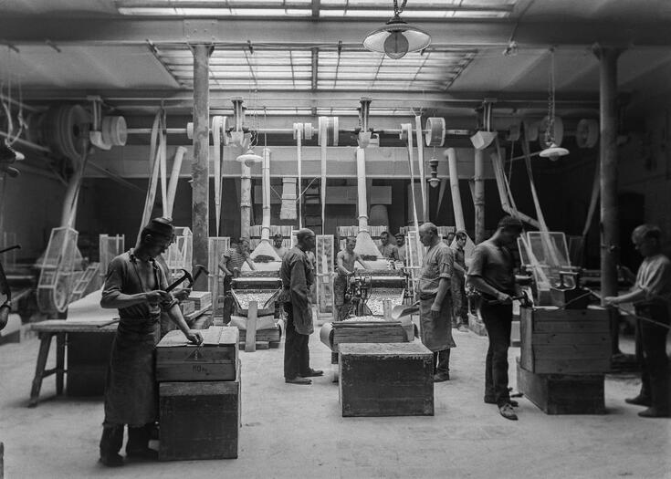 Flera män håller på att arbeta med att skära och förpacka socker i en ljus sal.