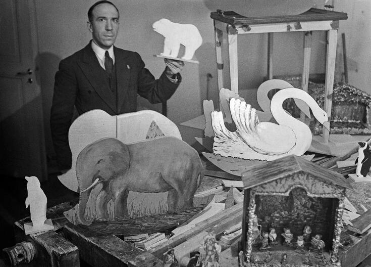 En man i mörk kostym visar upp leksaksdjur gjorda av trä: en björn, en svan och en elefant.