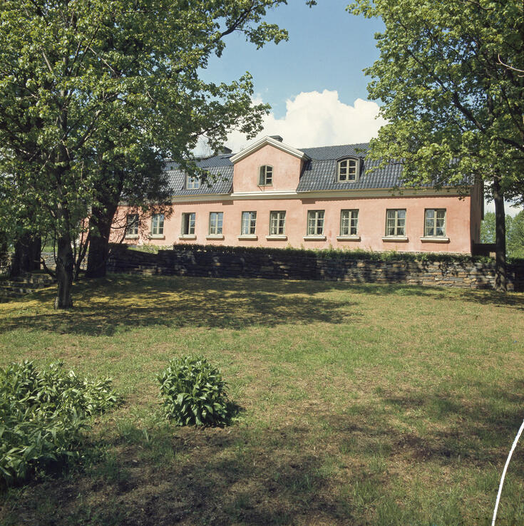 Vaaleanpunainen kaksikerroksinen kartanorakennus kuvattuna keällä.