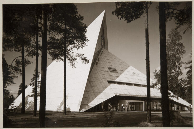 Hyvinge kyrkas fasad. Den kantiga, ljusa byggnaden ser ut att bestå av två pyramider som smälter ihop med varandra.