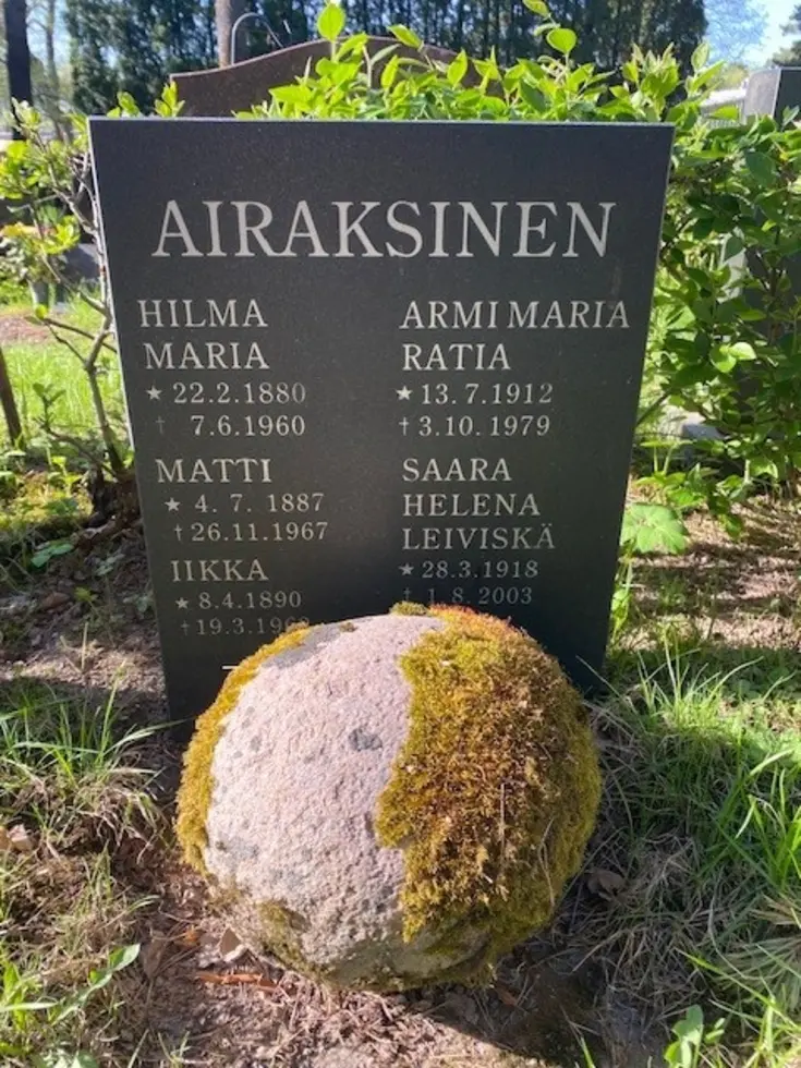 Mustassa yksinkertaisessa graniittipaadessa lukee AIRAKSINEN ja sen alla oikealla ARMI MARIA RATIA s. 13.7.1912, k. 3.10.1979