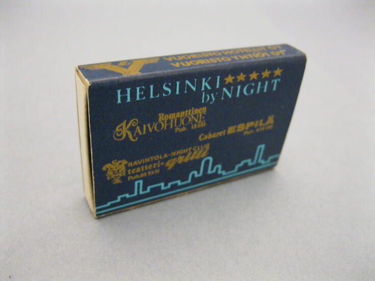 En kvadratisk, tunn tändsticksask i mörkblått med ljusblå text HELSINKI by NIGHT och en stiliserad siluett av staden i askens nedre kant. I mitten är tre gula restauranglogon. 