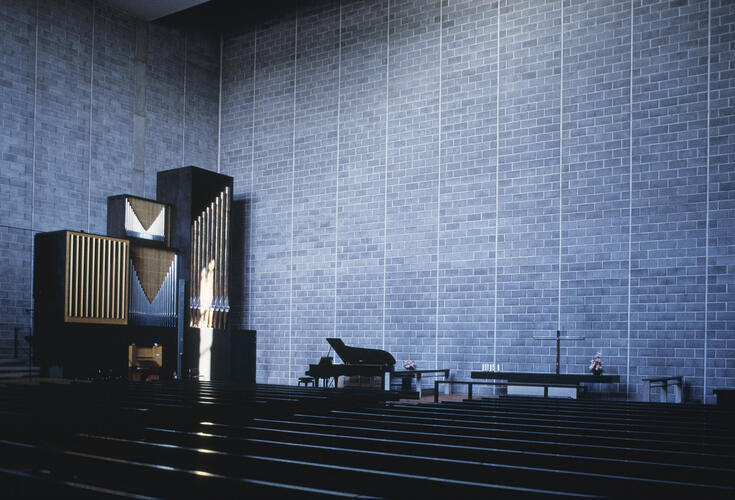 Kyrksalen i Hagalunds kyrka. Det höga, fyrkantiga rummet är dunkelt. Väggen består av ornamenterad betong.