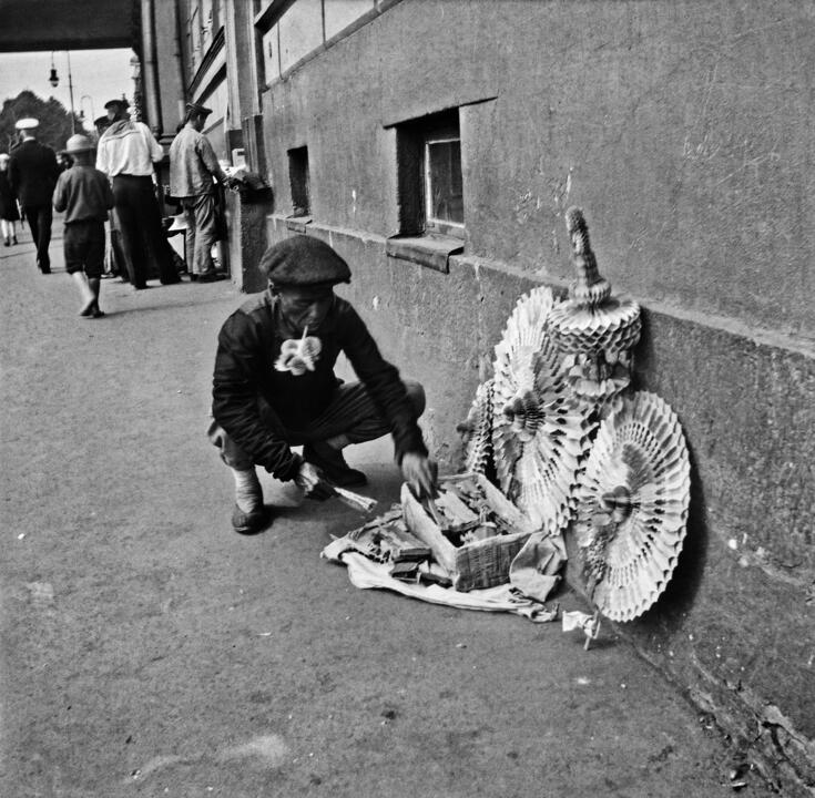 Aasialainen mies on kyykistynyt kadulle myymiensä koriste-esineiden viereen.