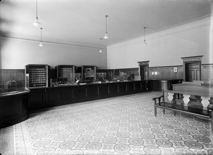 Fabianinkatu 15. Helsingfors Sparbank. Pankkisali ilman ihmisiä. Asiakaspalvelutiskillä on omat luukut veroja, lainoja ja rahatalletuksia varten. Keskellä salia on penkki asiakkaille.