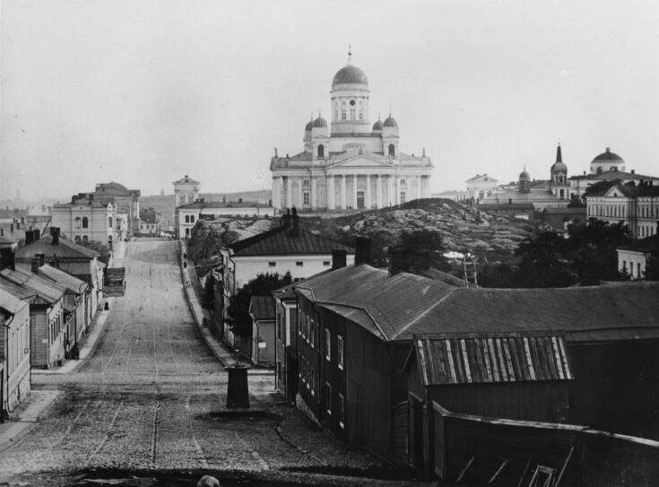 Kruununhaka. vas. Nikolainkatu (= Snellmaninkatu) 16-10 ja 27-15. Etualalla oikealla numero 8, entinen Nuuskamyllynmäki. Taustalla Nikolainkirkko. Matalia, enimmäkseen puisia rakennuksia, mukulakivikatu.