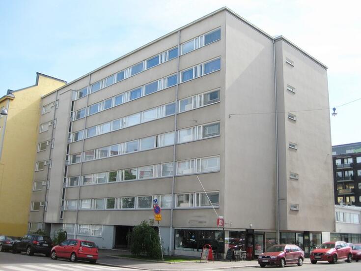 Harmaa, betoniseinäinen kerrostalo, jossa nauhaikkunat.