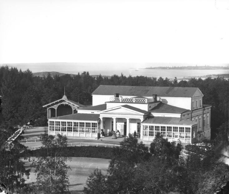A white large building surrounded by a park. Many columns on the porch.